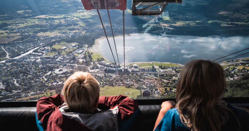 To born ser ut over Voss sentrum frå innsida av gondolen. Utsikta viser vatnet og det omliggande fjellandskapet.